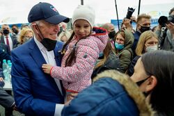 Photo of a smiling Biden holding a child, with a mask lowered onto his chin